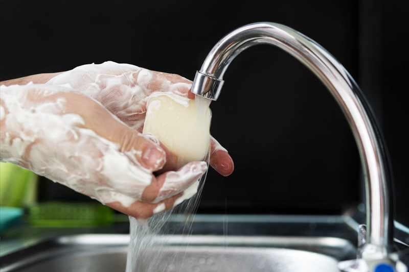 Close-up photo of hands lathered in suds, holding a bar of soap under a running tap